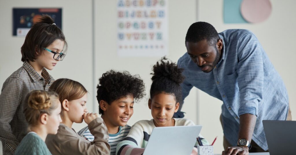 diverse group of children with male teacher using laptop together